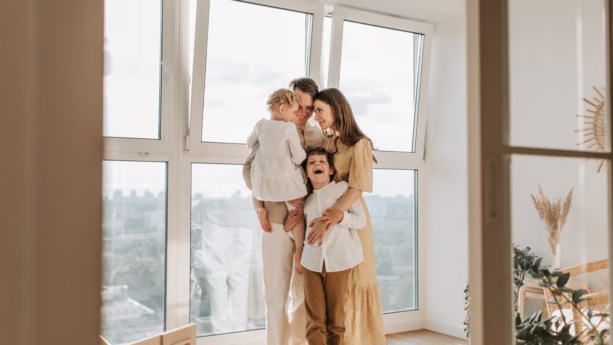 A loving family embraces near a large window in a bright, airy room, exuding warmth and togetherness.